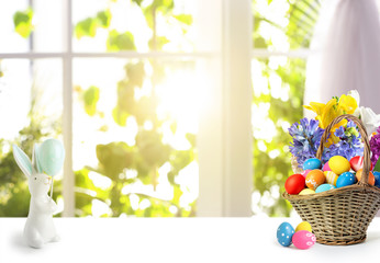 Bright Easter eggs in wicker basket and bunny figure on table indoors