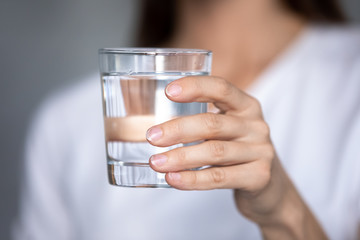 Close up focus on glass of pure distilled water in female hands. Young thirsty woman holding clear...