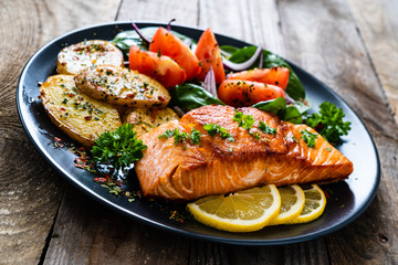 Fried salmon steak with potatoes and vegetables on wooden table
