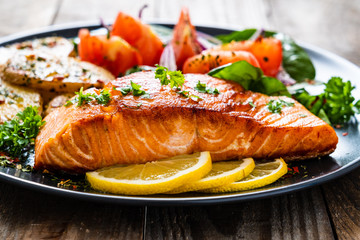 Fried salmon steak with potatoes and vegetables on wooden table
