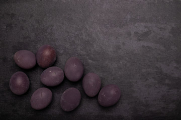 Dark easter eggs on stone table with black backdrop. Colored with wine.