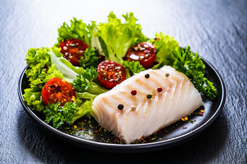 Fresh raw cod with vegetables on black stone board