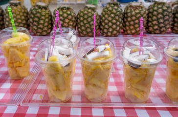 Fresh pineapple and coconut pieces in plastic transparent cups for sale at the farmers market