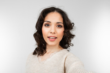 Fototapeta premium Beautiful brunette girl with makeup makes selfie on a gray studio background