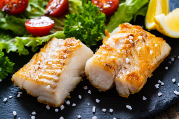 Fish dish - fried cod fillet with vegetables on wooden table