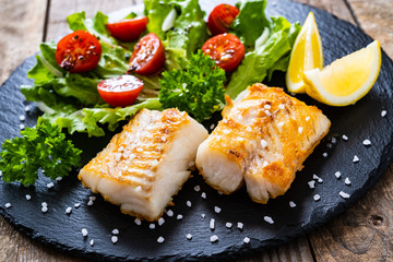 Fish dish - fried cod fillet with vegetables on wooden table