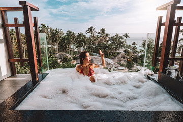 Asian woman relaxing in outdoor bath with tropical sea luxury spa hotel, lifestyle concept