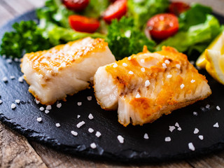 Fish dish - fried cod fillet with vegetables on wooden table