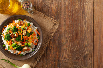 Tofu with rice and vegetables. Served on brown plate with chopsticks. Top view.
