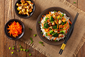 Tofu with rice and vegetables. Served on brown plate with chopsticks. Top view.