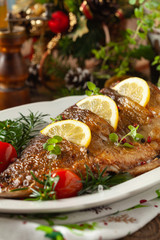 Fried carp whole. Served with lemon and cherry tomatoes on white plate. Christmas decoration.