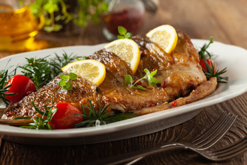 Fried carp whole. Served with lemon and cherry tomatoes on white plate. Christmas decoration.