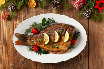 Fried carp whole. Served with lemon and cherry tomatoes on white plate. Christmas decoration. Top view.