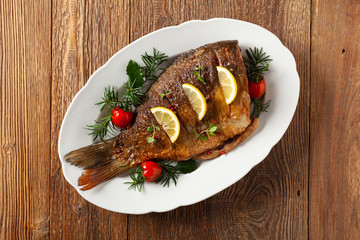 Fried carp whole. Served with lemon and cherry tomatoes on white plate. Christmas decoration. Top view.