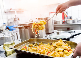 Chef cooks fried potatoes with pieces of meat in a restaurant kitchen