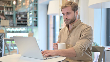 Man Holding Coffee Cup while Working on Laptop