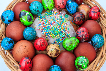 Fototapeta na wymiar Easter eggs painted in different colors and different sizes and Easter cake in a basket of twigs.