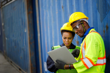 Male Engineer workers discussing with colleagues. Manual workers are wearing protective clothing They are standing against cargo containers.