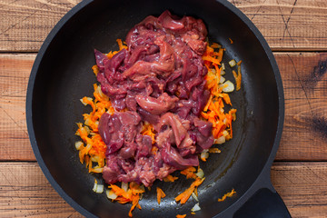 Step by step preparation of Farfalle with fried chicken liver and carrots, step 1 - adding raw chicken liver to fried carrots with onions, top view, horizontal