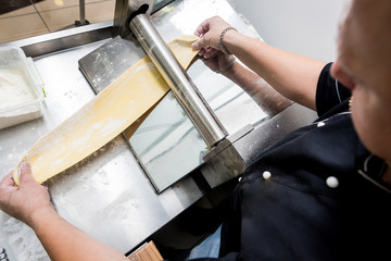 Chef rolling dough with a pasta machine. Pasta maker machine. Hom