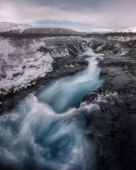 The Icelandic Bruarfoss waterfall with its characteristic blue color on a cold winter day with completely snowy surroundings