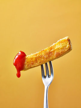 A chip dipped in tomato sauce on a fork against a yellow background