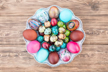 Plate with Easter eggs painted in different colors and different sizes on a wooden unpainted table