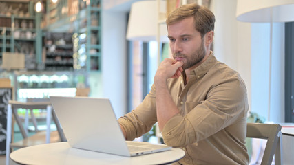 Pensive Young Man using Laptop in Cafe