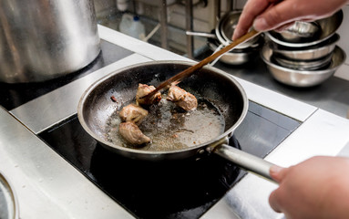 Chef cooks fried potatoes with pieces of meat in a restaurant kitchen
