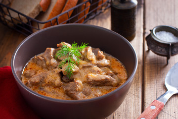 Traditional beef stroganoff in a ceramic bowl on a wooden table, selective focus