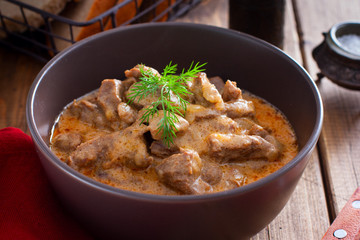 Traditional beef stroganoff in a ceramic bowl on a wooden table, selective focus