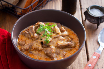 Traditional beef stroganoff in a ceramic bowl on a wooden table, selective focus