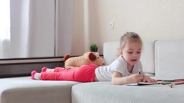 Four years little girl with pretty face concentrated girl draw color pencil lying on the sofa, children playtime education concept.