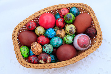 Fototapeta premium Basket of straws with Easter eggs painted in different colors and different sizes on a tablecloth