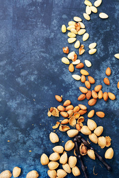 Almonds in shells,  almonds kernals and blanched almonds scattered on a textured blue background.