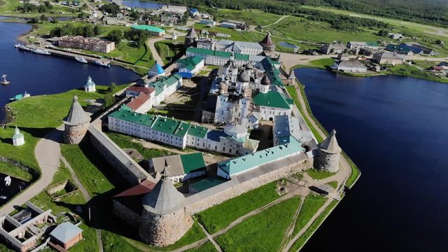 Smooth cinematic flyby of the Solovetsky monastery from the south side with a view of the White sea, Saint Lake and nearby village on a clear sunny day with contrast lighting.