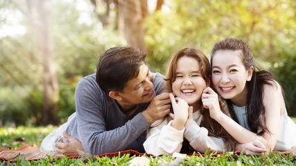 Asian family has Father and mother hugging their daughters, happy with a smile in the park.