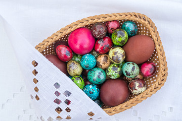 Basket of straws with Easter eggs painted in different colors and different sizes  on a tablecloth