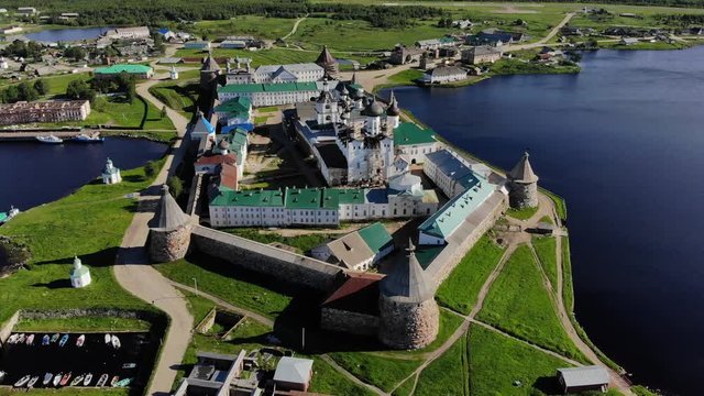 Smooth cinematic flyby of the Solovetsky monastery from the south side with a view of the White sea, Saint Lake and nearby village on a clear sunny day with contrast lighting.