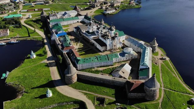 Smooth cinematic flyby of the Solovetsky monastery from the south side with a view of the White sea, Saint Lake and nearby village on a clear sunny day with contrast lighting.