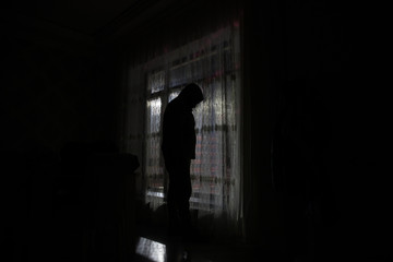 Silhouette of a man standing at a window inside the room. Fantasy picture with old vintage lantern at the window inside dark room.