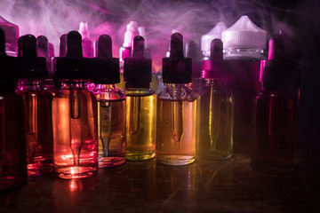 Smoke clouds and vape liquid bottles on dark background. Light effects. Useful as background or...