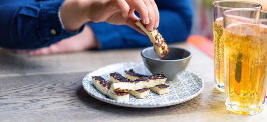 Young woman eating Halloumi grilled cheese and drinking beer. Healthy halloumi cheese and salsa in the restaurant. Woman healthy halloumi grilled greek  cheese. Healthy diet of Mediterranean food. 