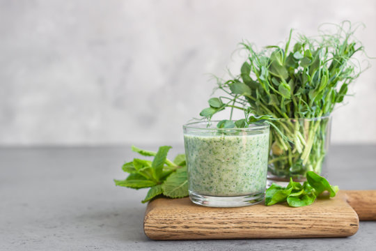 Green smoothie with spinach, mint and young sprout microgreen on a wooden board, grey stone background. Healthy food concept.