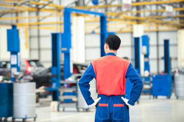 The back image of the male car mechanic in the car service center in the background of the service. Concept: Machine repair, error diagnosis, expert, technical maintenance.