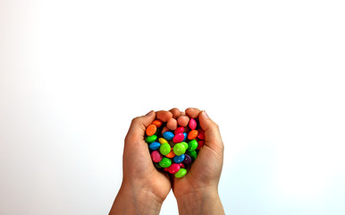 small multi-colored sweets in children's hands on a white background