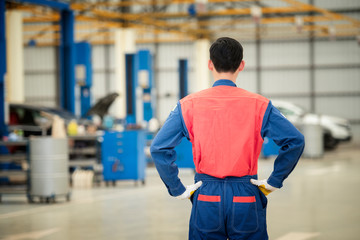 The back image of the male car mechanic in the car service center in the background of the service. Concept: Machine repair, error diagnosis, expert, technical maintenance.