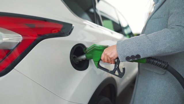 Woman fills petrol into her car at a gas station close-up.
