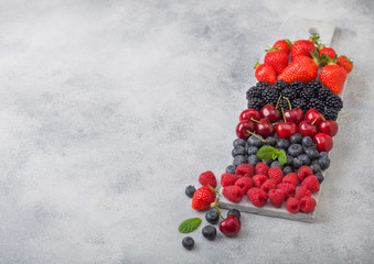 Fresh organic summer berries mix on white marble board on light kitchen table background. Raspberries, strawberries, blueberries, blackberries and cherries. Space for text