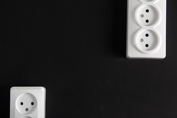 Two white sockets in different edges of the black wall.
